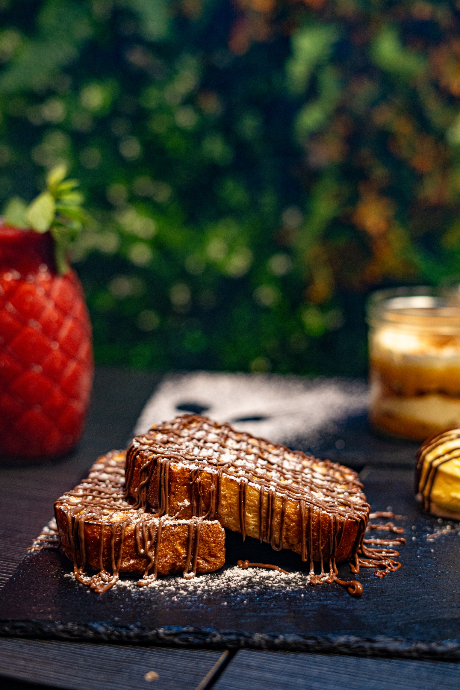 Tranches de gâteau croustillantes décorées avec du sucre glace, accompagnées d'un dessert crémeux en verrine et d'une décoration élégante en arrière-plan.
