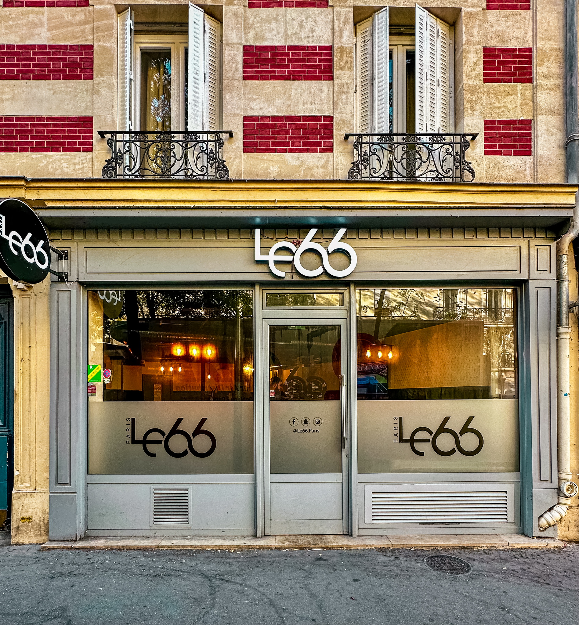 Façade du bar Le 66 avec son logo distinctif, situé dans un immeuble parisien élégant avec des balcons en fer forgé.